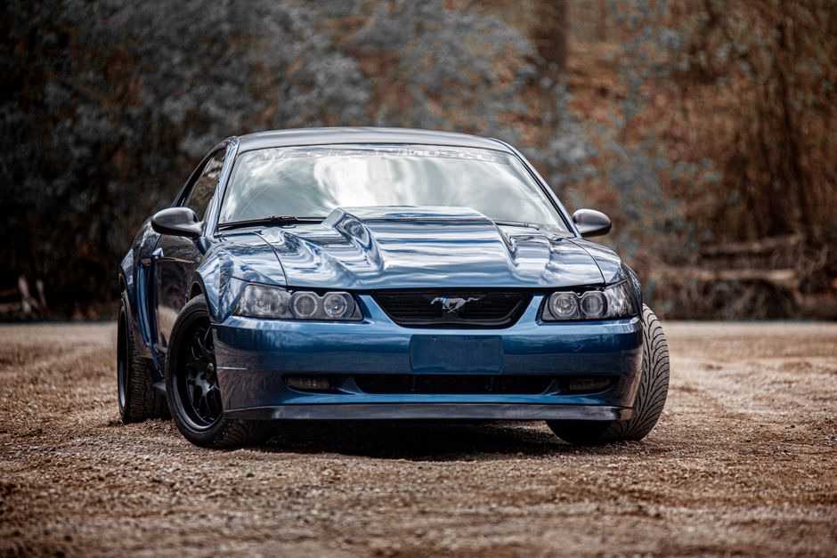 A blue Ford Mustang parked outdoors surrounded by a natural forest setting.