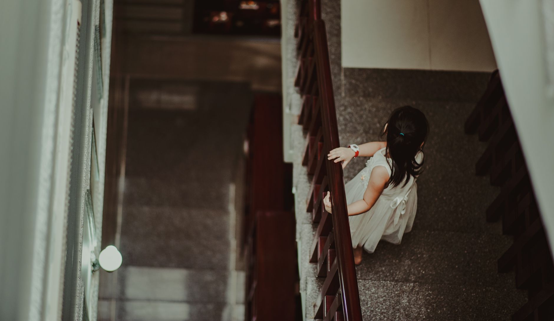 A young girl in a white dress gracefully ascending a staircase, captured indoors.