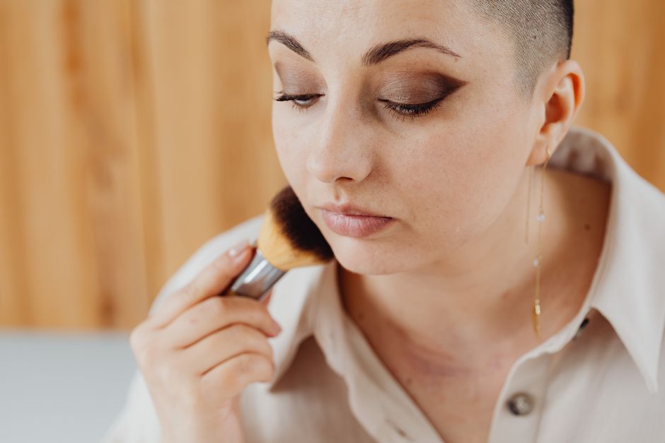 A woman applying makeup with a brush in a detailed face shot, highlighting makeup artistry.