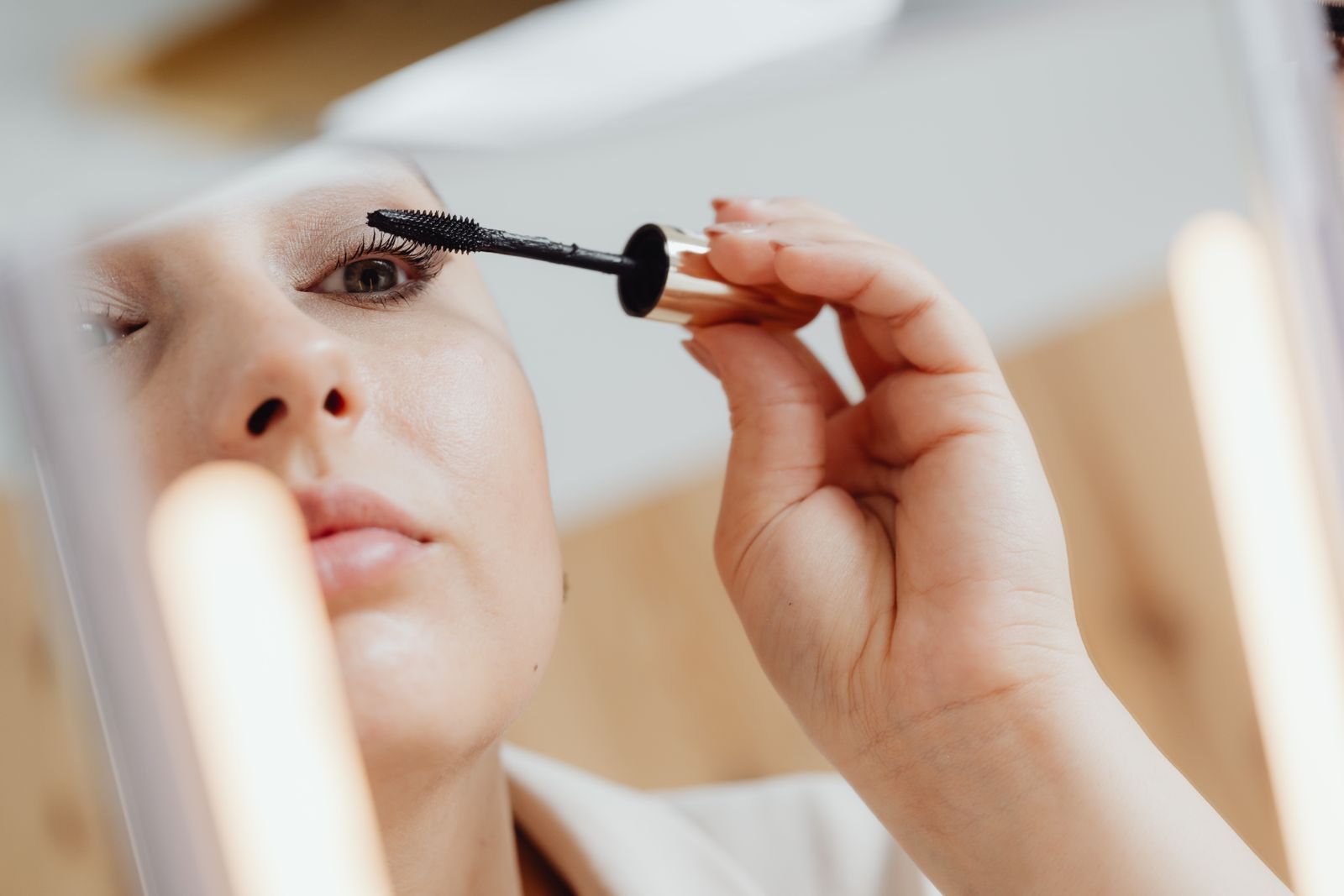 Woman applying mascara close to the lash line in a mirror with bright bathroom lighting