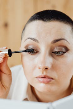 A woman with short hair applies mascara, demonstrating a modern makeup routine.