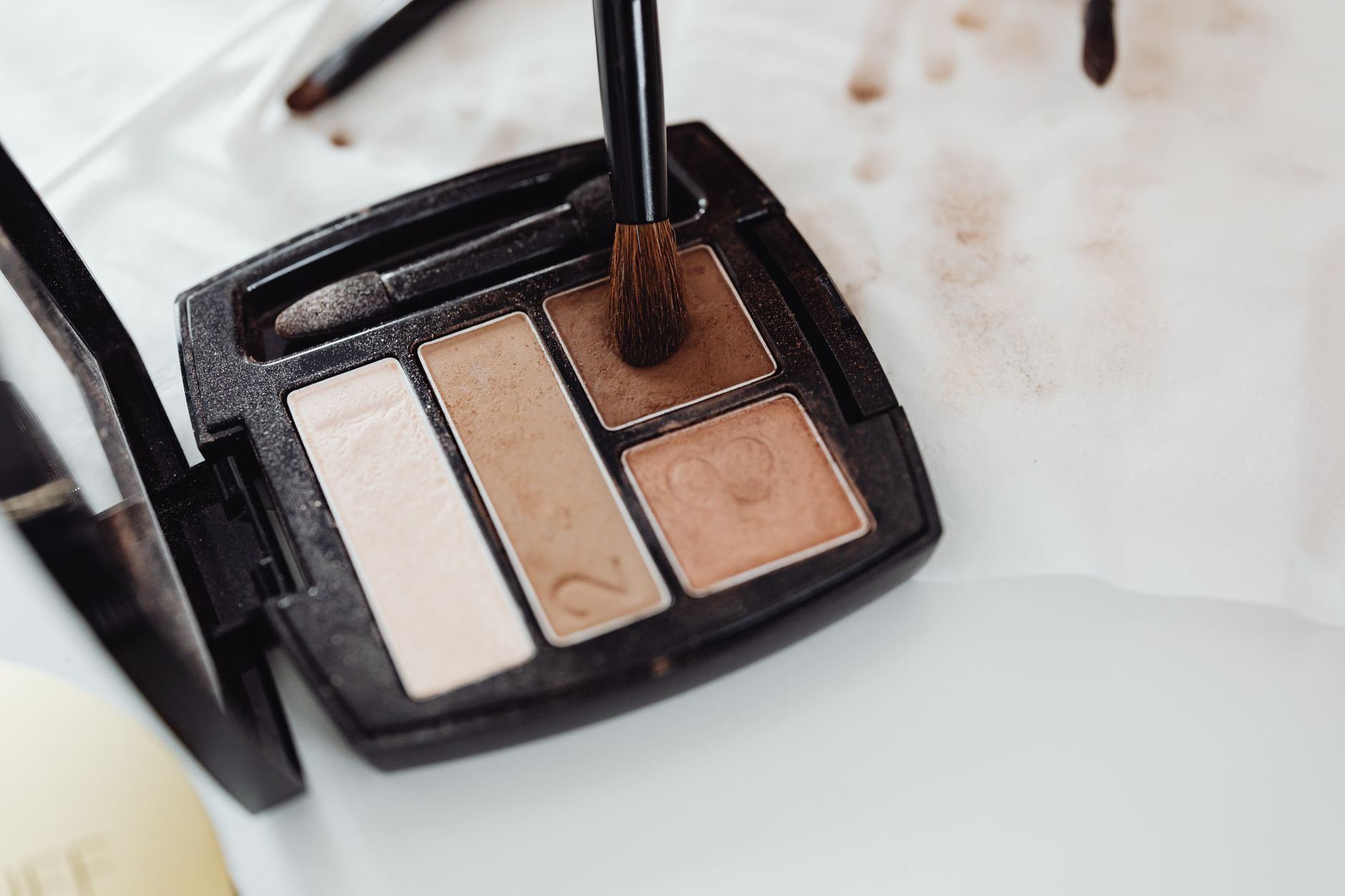 Close-up of a makeup eyeshadow palette in neutral shades with a brush touching the product surface.