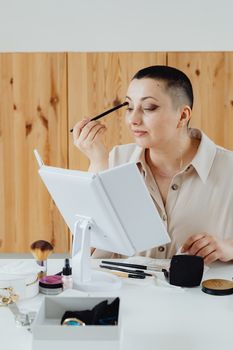 A woman focuses on applying eyeshadow while using a makeup mirror at home.