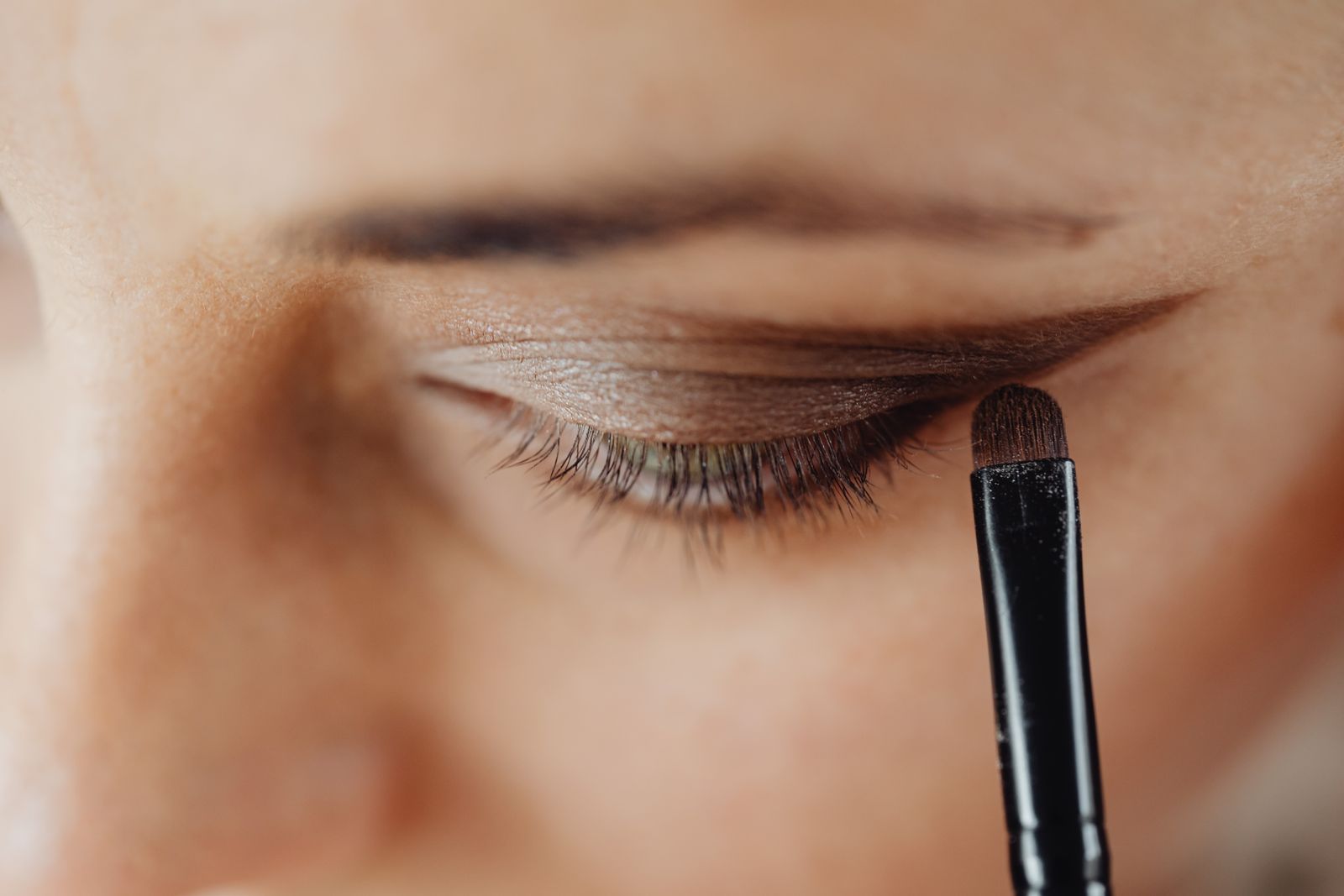 Gros plan sur un œil bleu maquillé en nuances cuivrées avec fard chaud et mascara brun