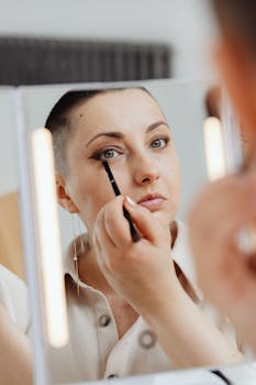 Close-up portrait of woman applying eyeliner with focus on reflection in the mirror.