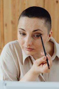 Woman applying eyeshadow with a makeup brush in a well-lit room, showcasing simple beauty routine.