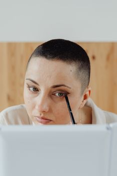 Woman with short hair applying makeup in front of a mirror indoors.