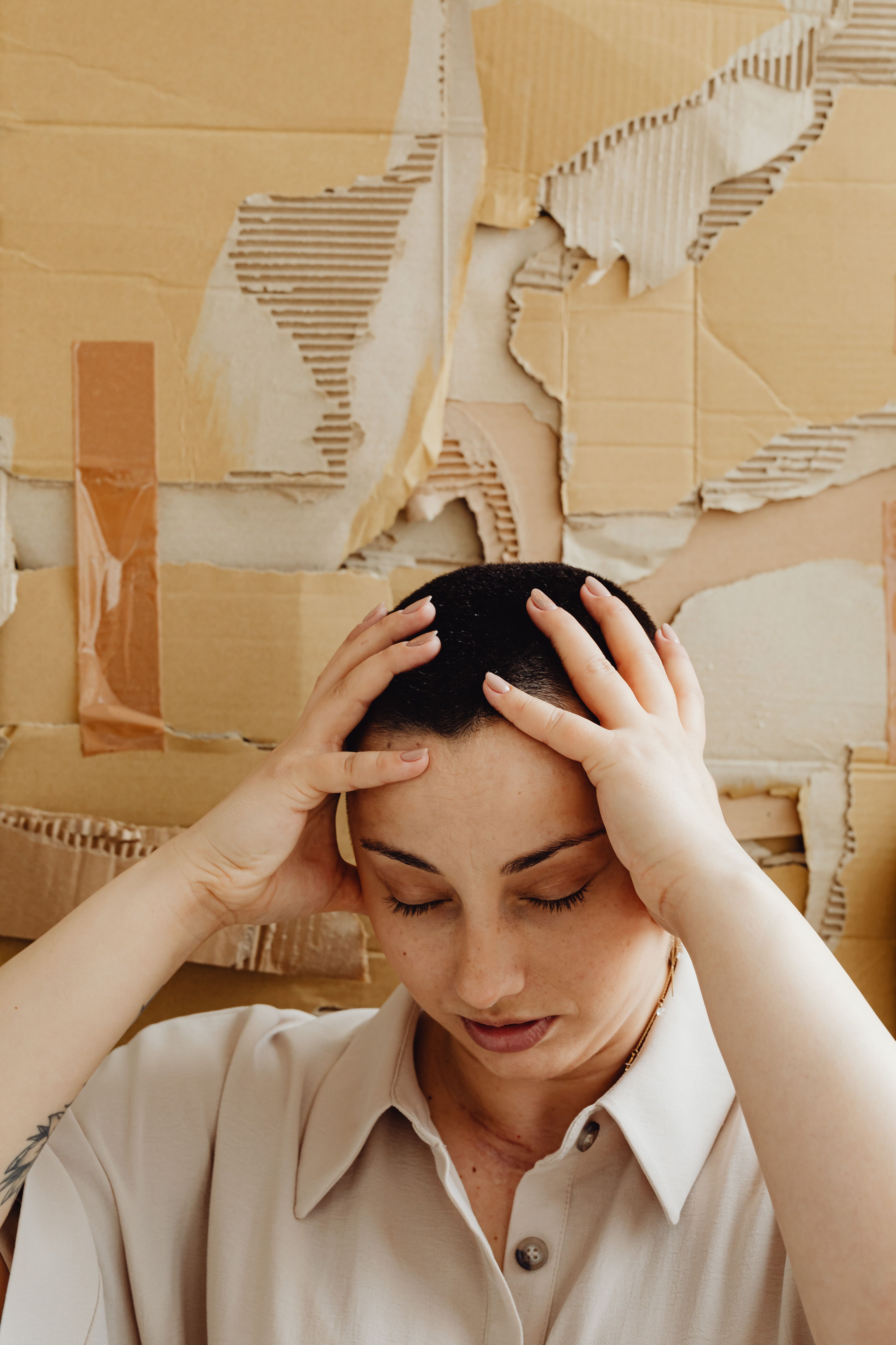 Portrait of a stressed woman holding her head against a cardboard wall backdrop.