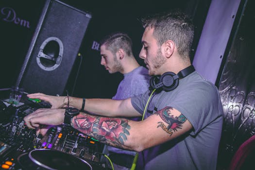 Two DJs mixing music at a vibrant nightclub, showcasing tattoos and DJ equipment.