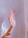 Crop faceless lady demonstrating hand with wavy sunbeams near white wall in bright room