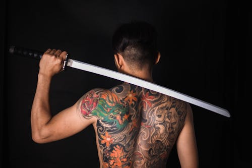 Back view of anonymous male with tattoos and naked body on black background of studio