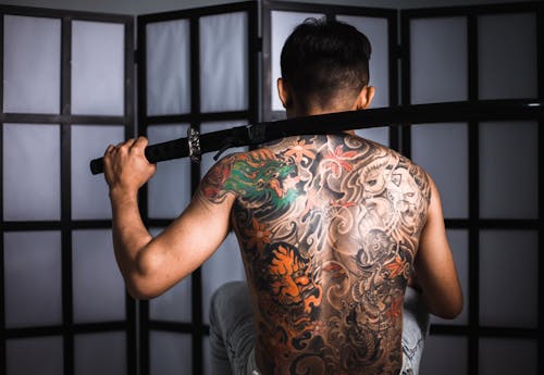 Back view of anonymous male with heavy katana in hand and tattoos near screen