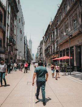 People walking along a vibrant street in Mexico City with historic buildings and the Torre Latinoamericana in the background.