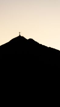 A breathtaking silhouette of a mountain peak with a cross at sunset, creating a serene and spiritual scene.
