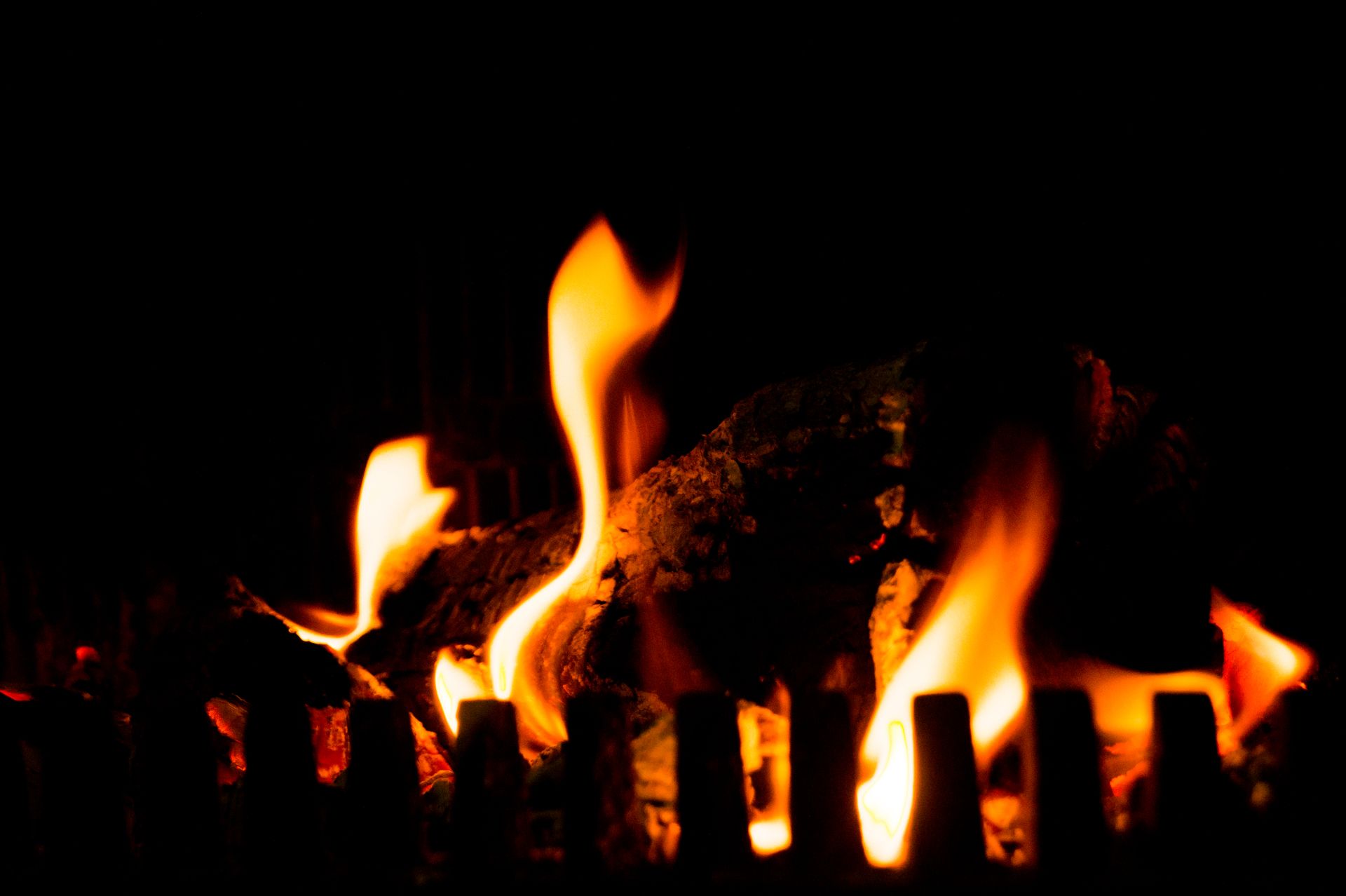 Close-up of a burning log in a dark, cozy fireplace setting with vivid flames.