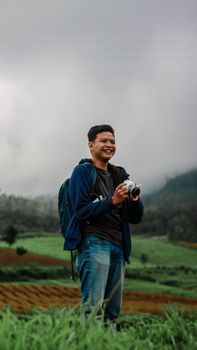 A joyful photographer capturing moments in a lush, cloudy Indonesian landscape.