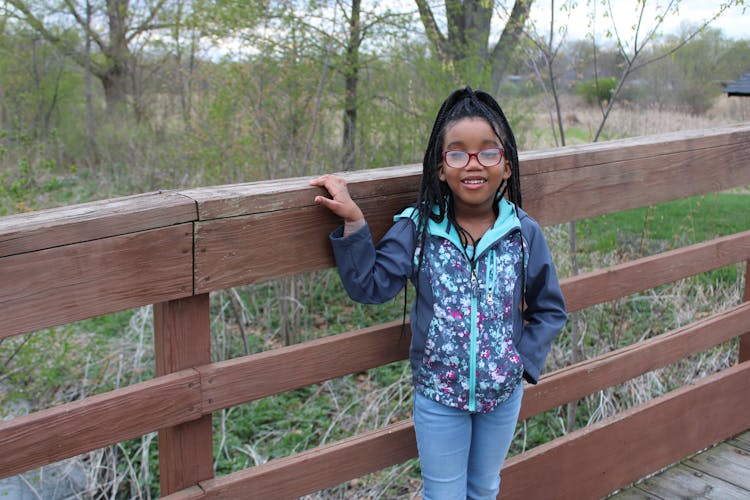 Child Standing Beside A Wooden Fence