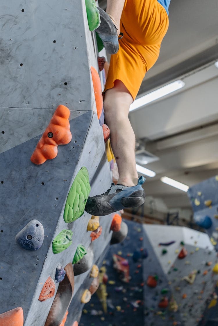 A Man In Orange Shorts Stepping On Climbing Holds