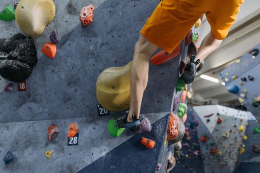 Adult male climber in orange shorts scaling an indoor bouldering wall.