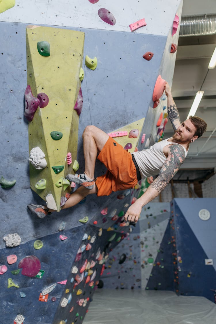 A Man In White Sleeveless Shirt And Orange Short Rock Wall Climbing