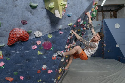 A tattooed man climbing on an indoor bouldering wall, embodying focus and fitness.