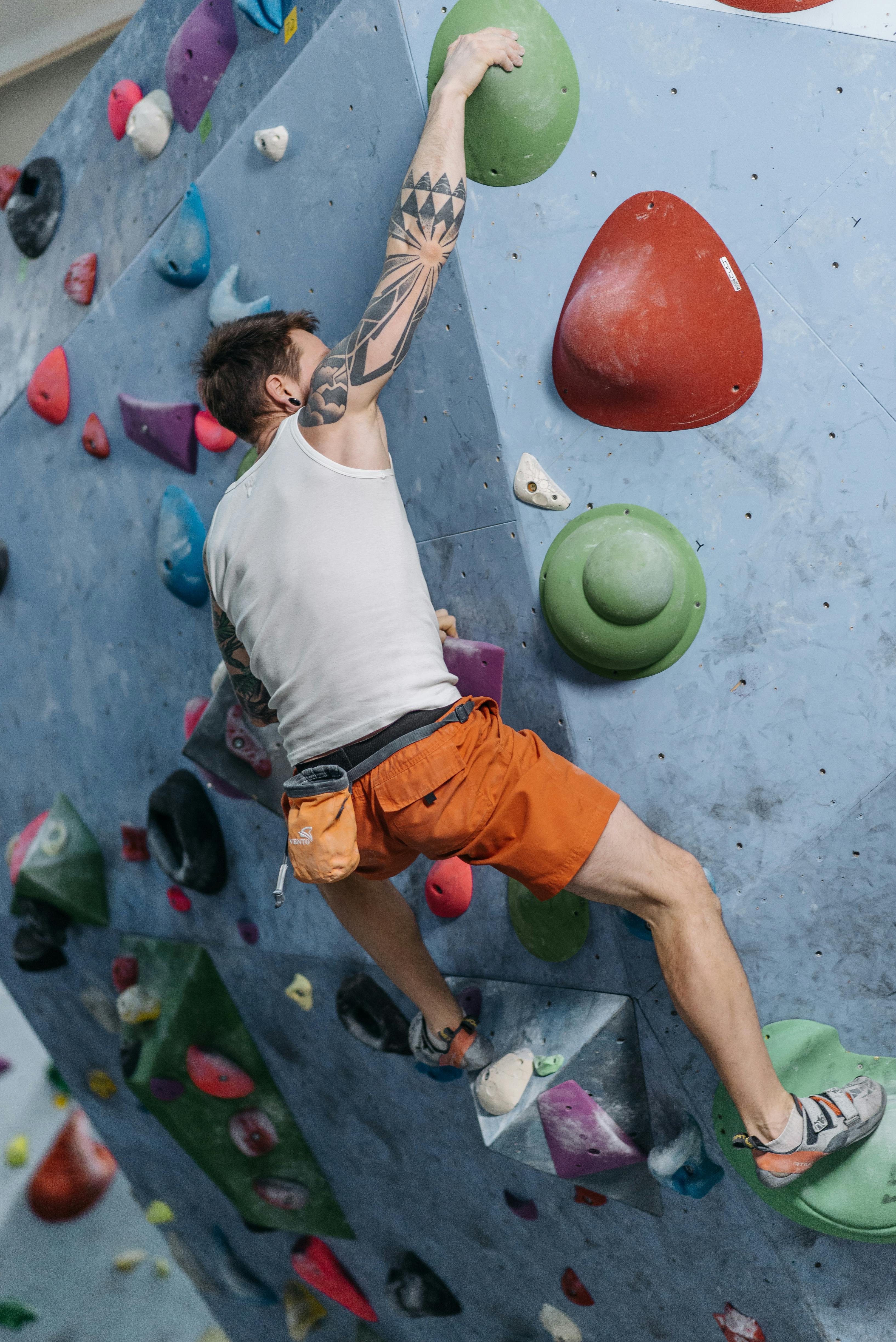 Adult man rock climbing indoors on a colorful climbing wall.