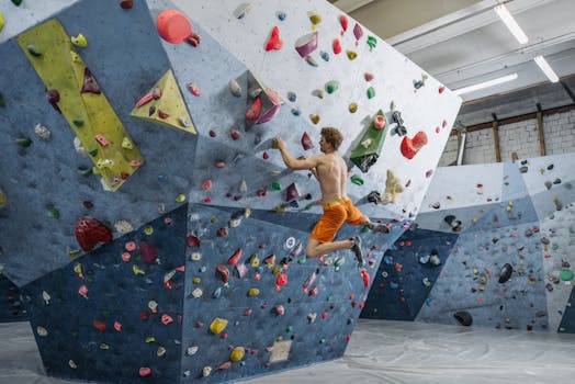 Shirtless man climbing an indoor rock wall with colorful holds, showcasing strength and athleticism.