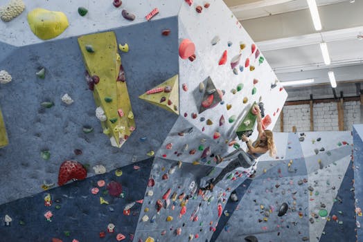 A woman skillfully maneuvers a challenging indoor bouldering wall.