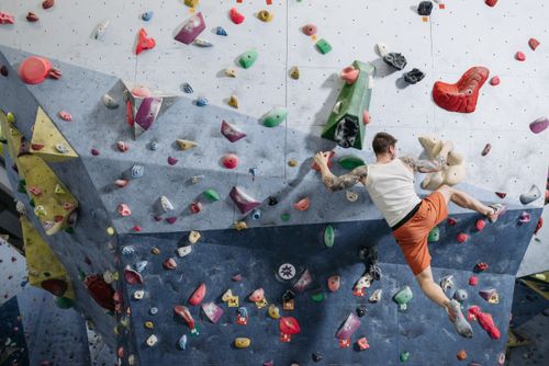 Free Adult male rock climber scaling a colorful indoor climbing wall, showcasing athleticism and focus in a dynamic setting. Stock Photo