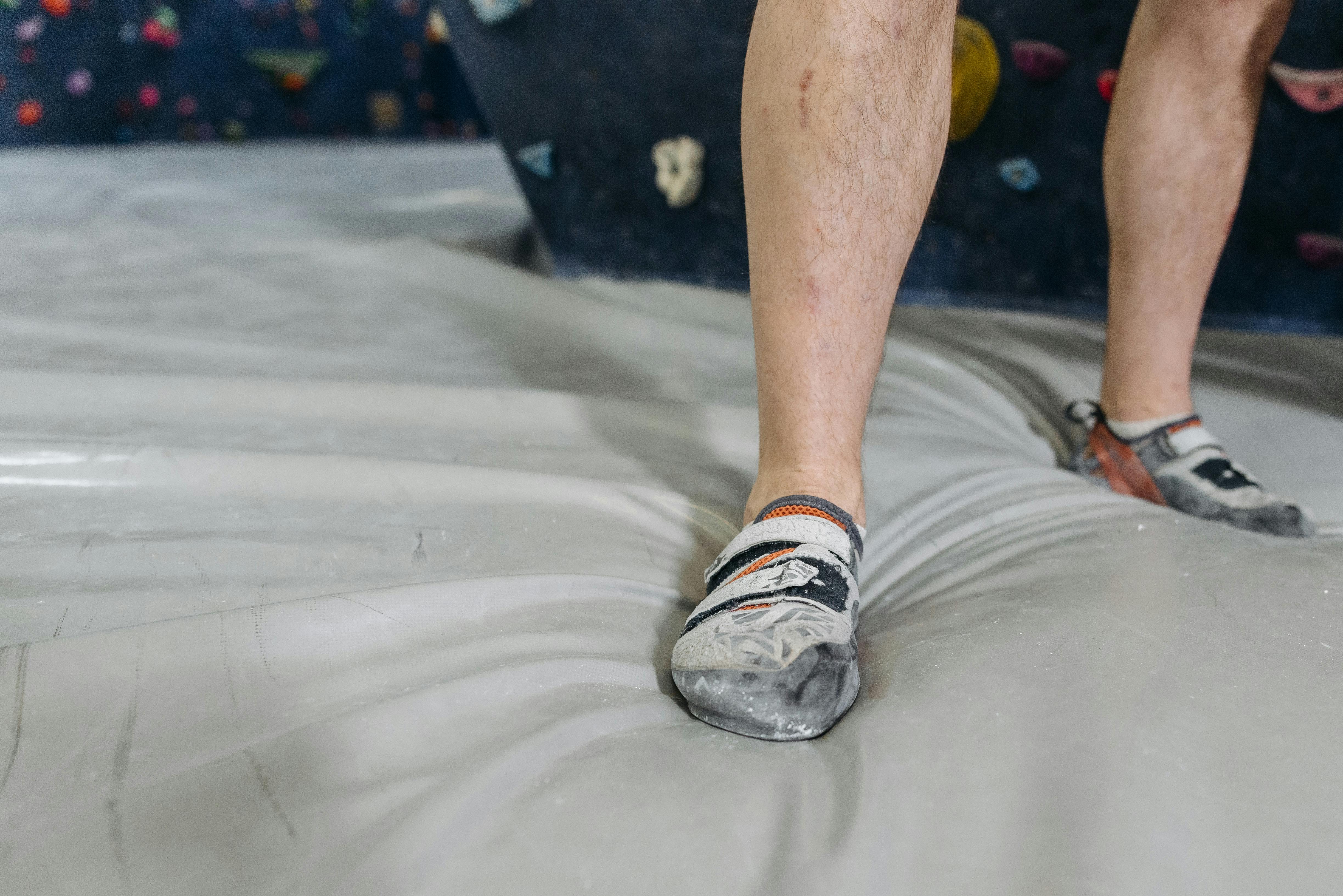 A climber's legs in climbing shoes on a gym floor, close-up view.