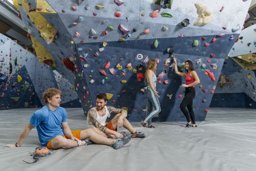 A diverse group of friends relaxing and climbing at an indoor climbing gym.