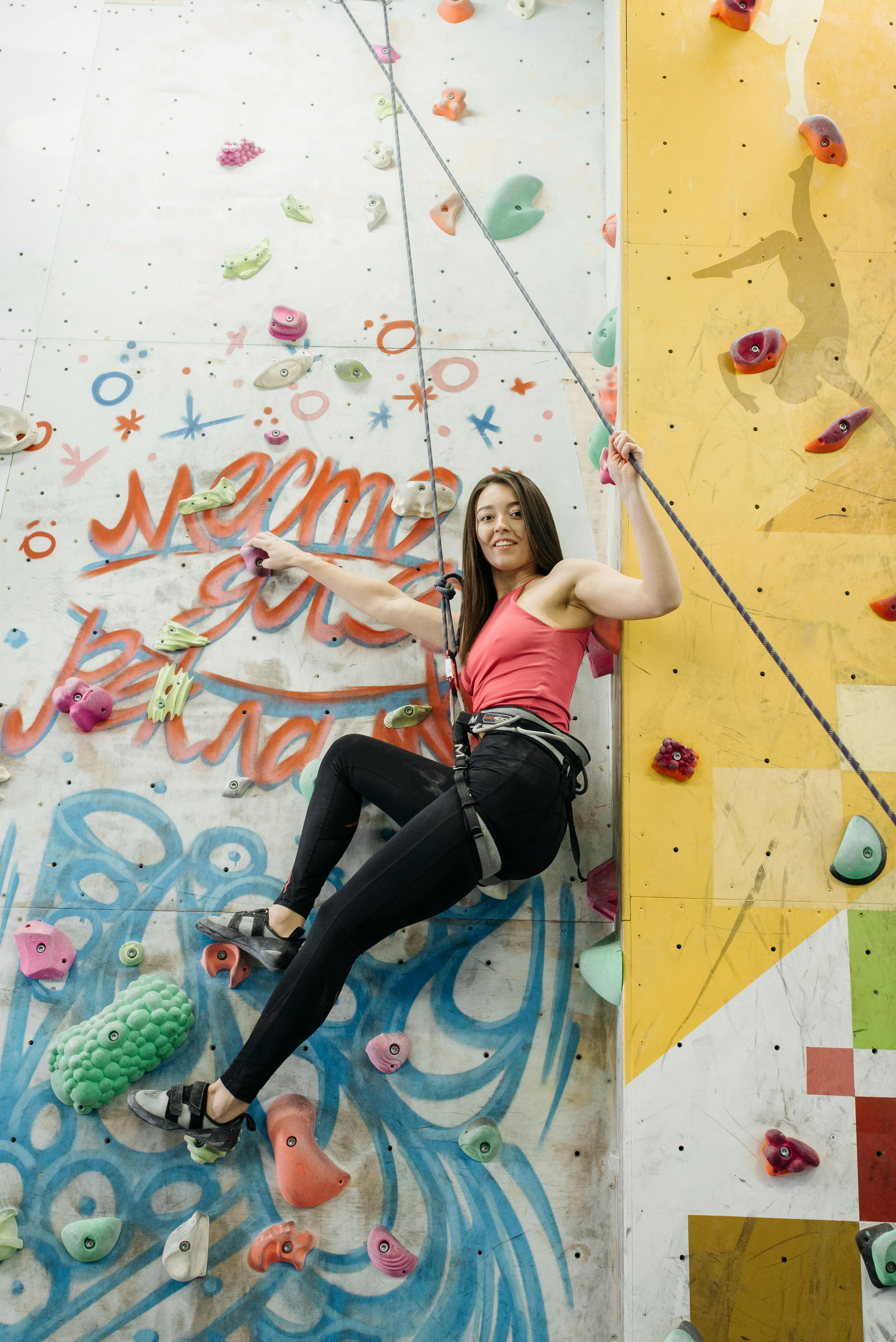 A woman in activewear rock climbing indoors, showcasing strength and balance.