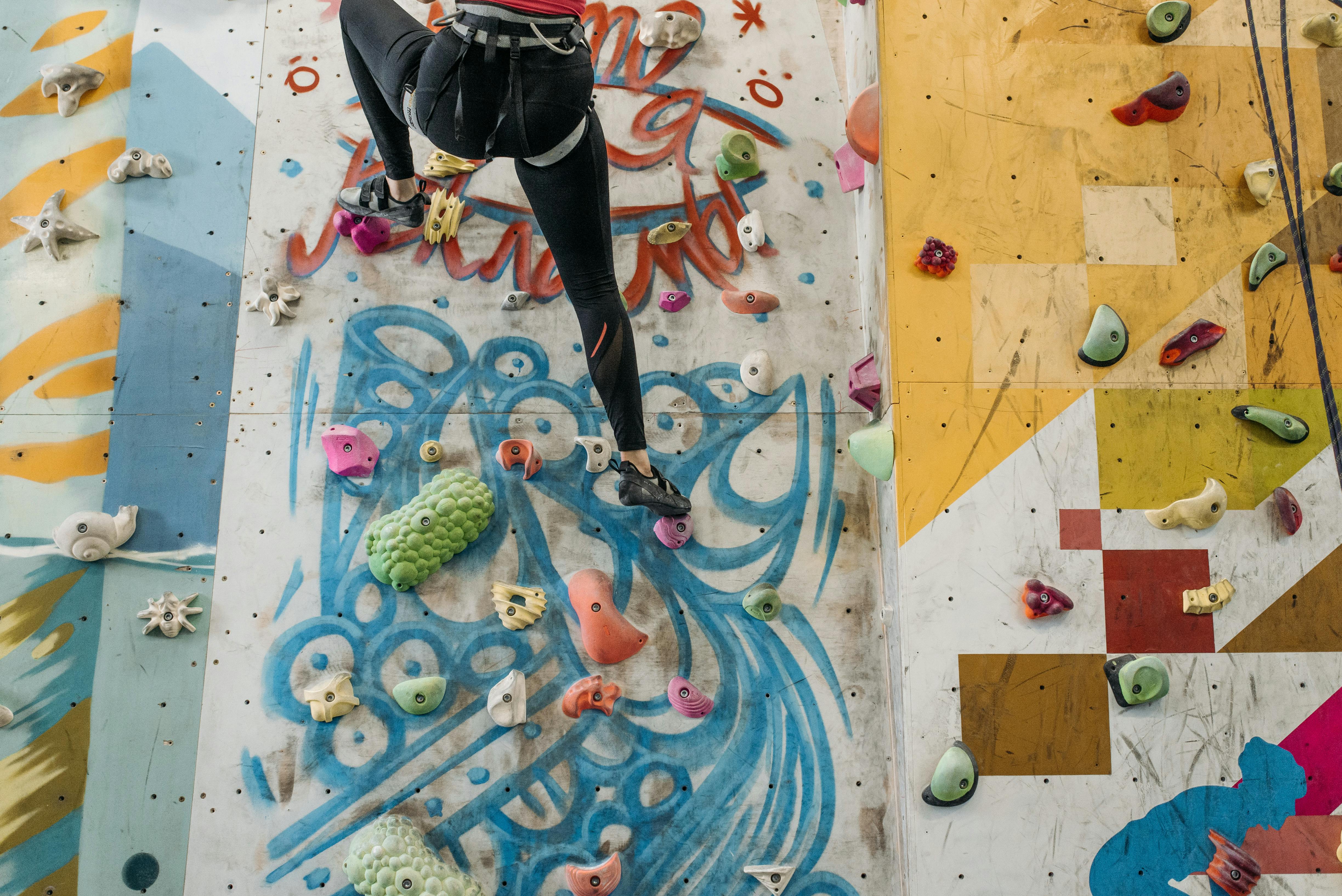 A climber scales a colorful indoor rock climbing wall with various holds.