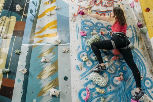 Free Woman climbs a vibrant graffiti indoor rock wall, showcasing strength and determination. Stock Photo