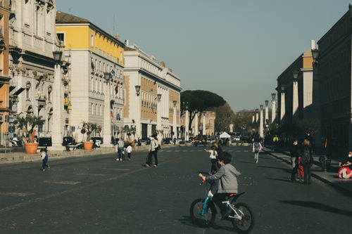 Free Unrecognizable children with parents on asphalt roadway between aged building exteriors and lanterns in town on sunny day Stock Photo
