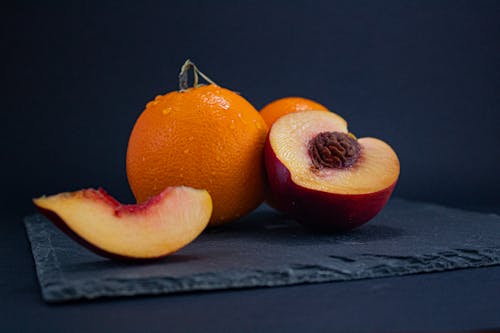 Close-Up Photo of an Orange Beside a Peach Fruit