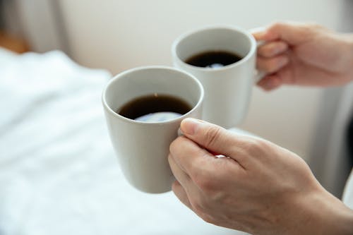 Free Close-Up Photo of a Person's Hands Holding Two Mugs of Black Coffee Stock Photo