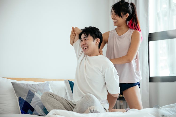 Cheerful Asian Couple Training Yoga In Bed At Morning Sunlight