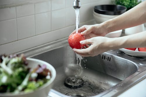 Person Washing an Apple in the Kitchen Sink