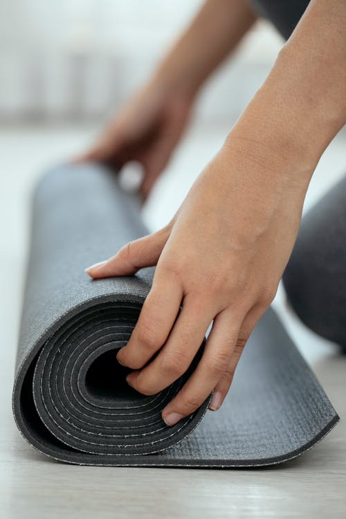 Free Crop female holding rolled mat on floor Stock Photo