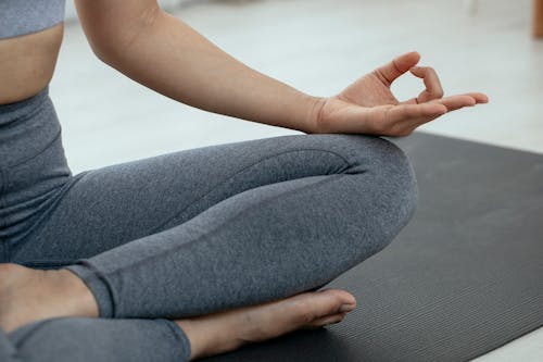 Crop unrecognizable person in sportswear sitting on floor and meditating in lotus pose during yoga session
