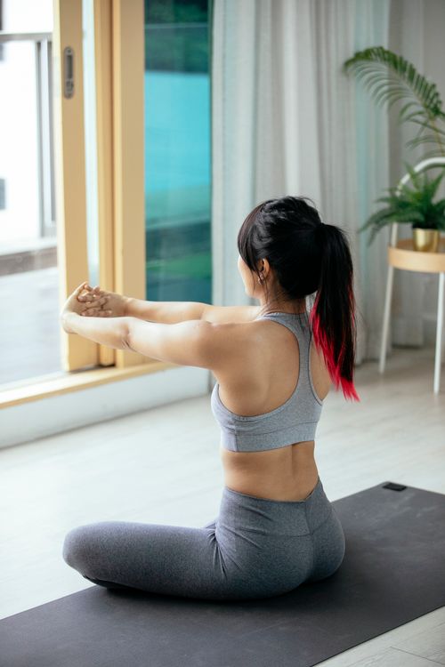 Free Unrecognizable slim female in activewear stretching arms while sitting on floor during fitness in spacious room in daytime Stock Photo