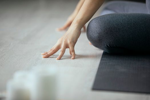 Crop unrecognizable female in gray leggings sitting on mat in Padmasana position and touching floor while doing yoga