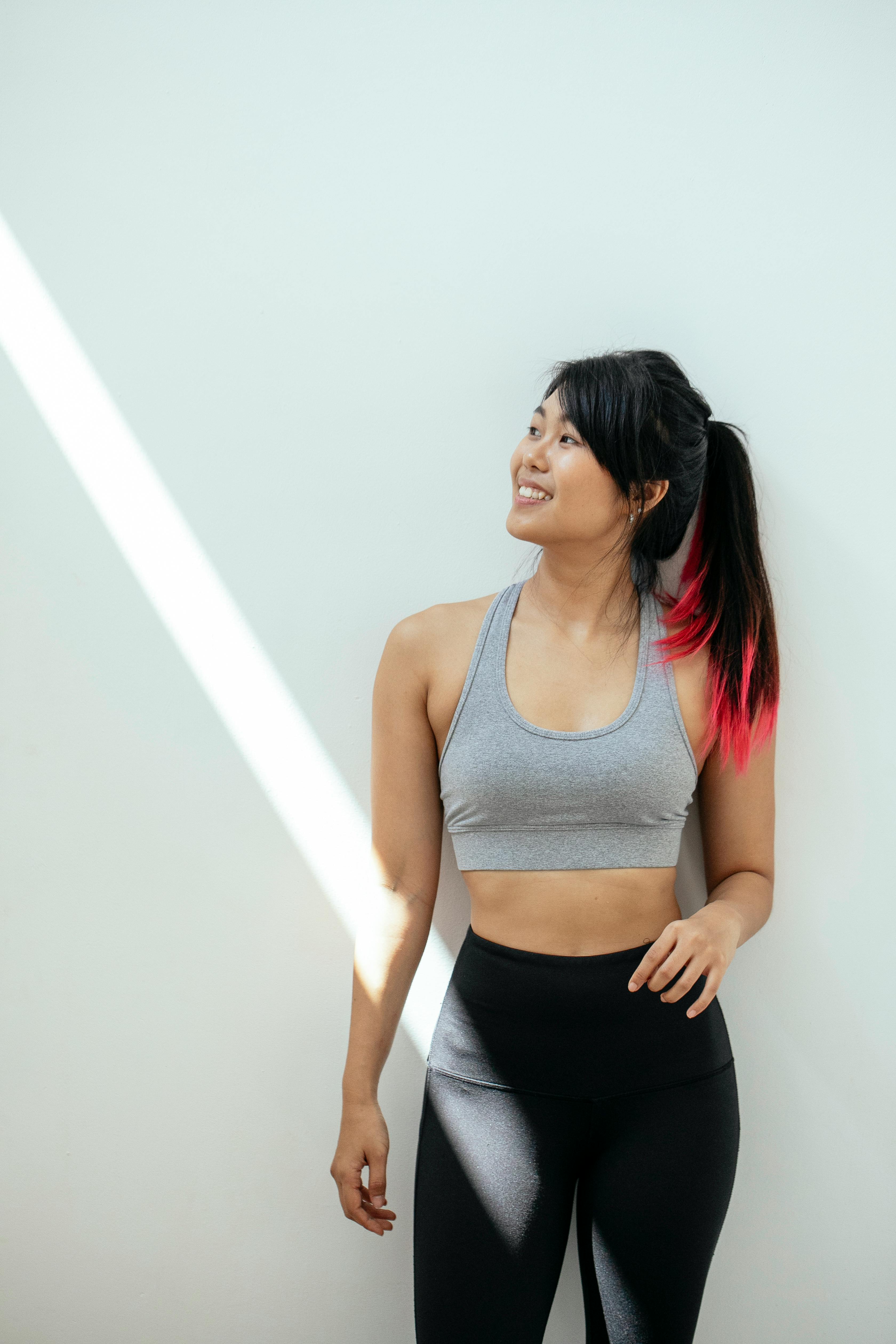 Smiling woman in sportswear leaning against a sunlit wall — your webinar coach