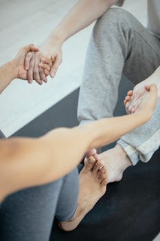 From above of crop unrecognizable people in sportswear doing exercise together while sitting on mat in daylight