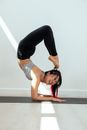 Full body of smiling young Asian female doing Scorpion pose while practicing Vrischikasana A yoga pose on mat in light room in sunlight