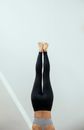 Crop anonymous fit female in gray top and black leggings preforming upside down pose of Handstand yoga asana