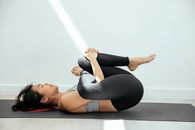 Fit Asian woman lying on yoga mat in cradle pose