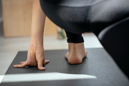 Back view of crop unrecognizable flexible female stretching legs and practicing yoga in Crescent Lunge on the Knee pose at home