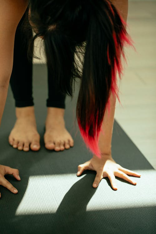 Free Crop anonymous woman standing on mat in Uttanasana position while practicing yoga Stock Photo